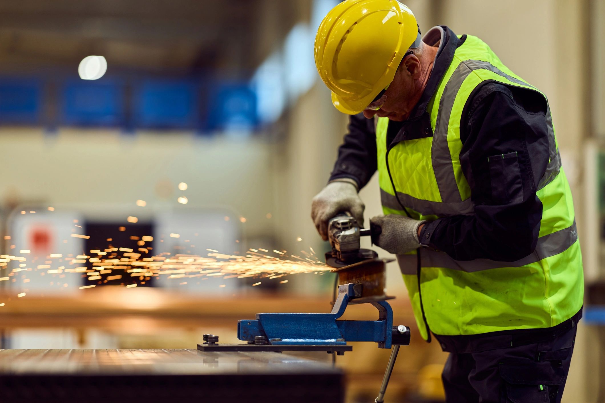 Industrial Worker Grinding Metal In Factory Workshop Wearing Safety Helmet And High-Visibility Vest
